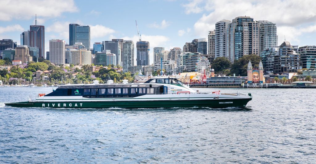 A Rivercat vessel cruising in Sydney Harbour with buildings in the background